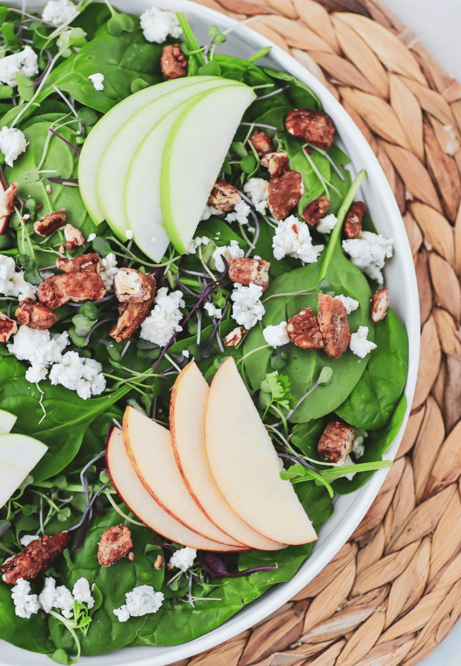 Spinach salad with sliced apples, pecans and blue cheese crumbles on a braided plate charger.