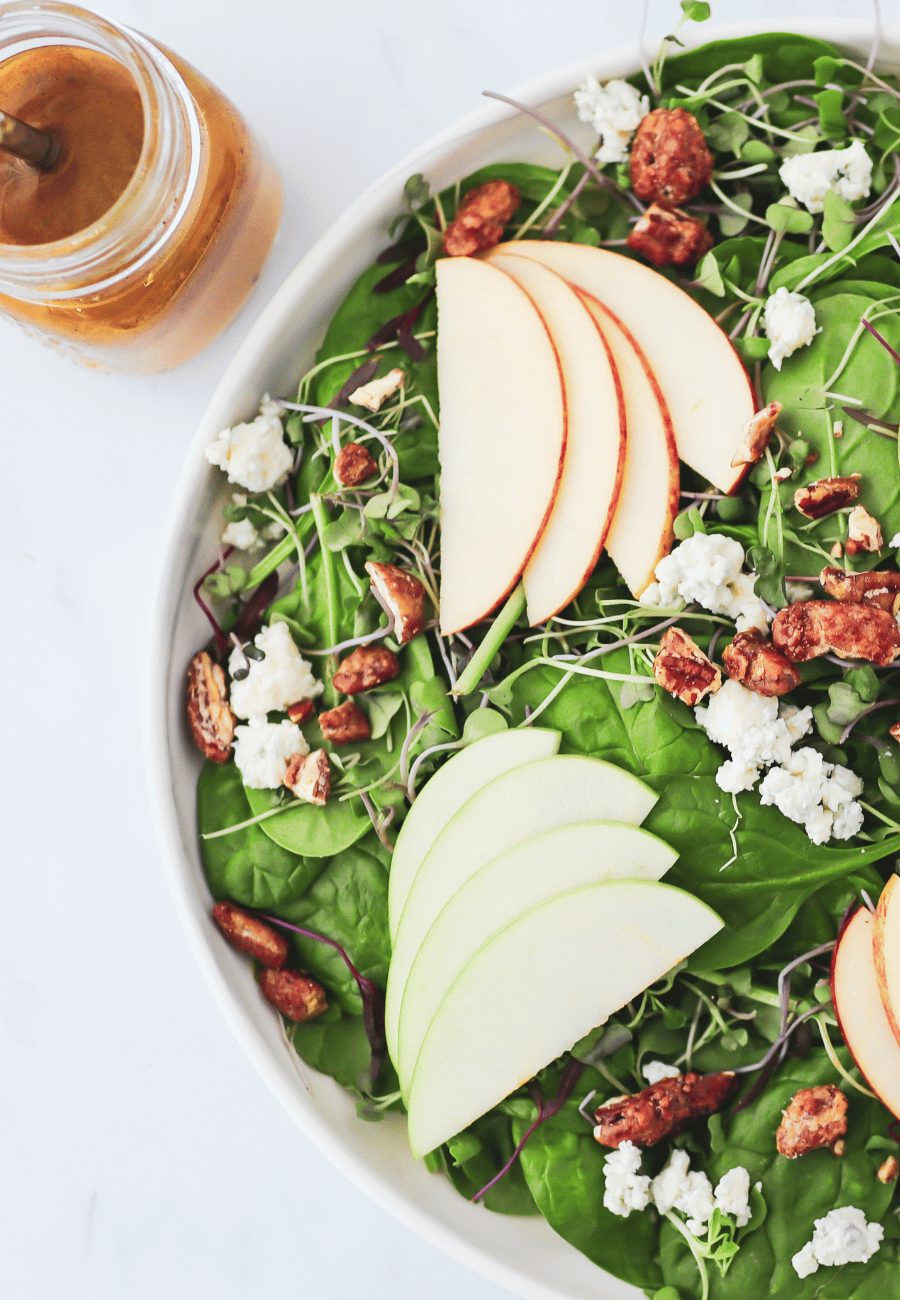Salad bowl with sliced apples, pecans and blue cheese crumbles and a side of vinaigrette