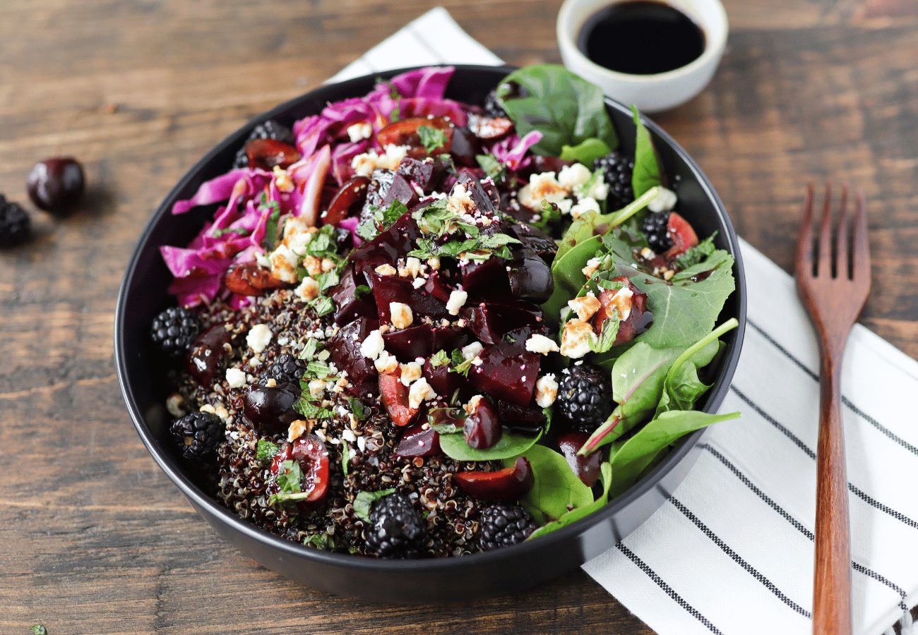 Grain bowl with purple cabbage, quinoa, greens, roasted beets, dark cherries and blackberries