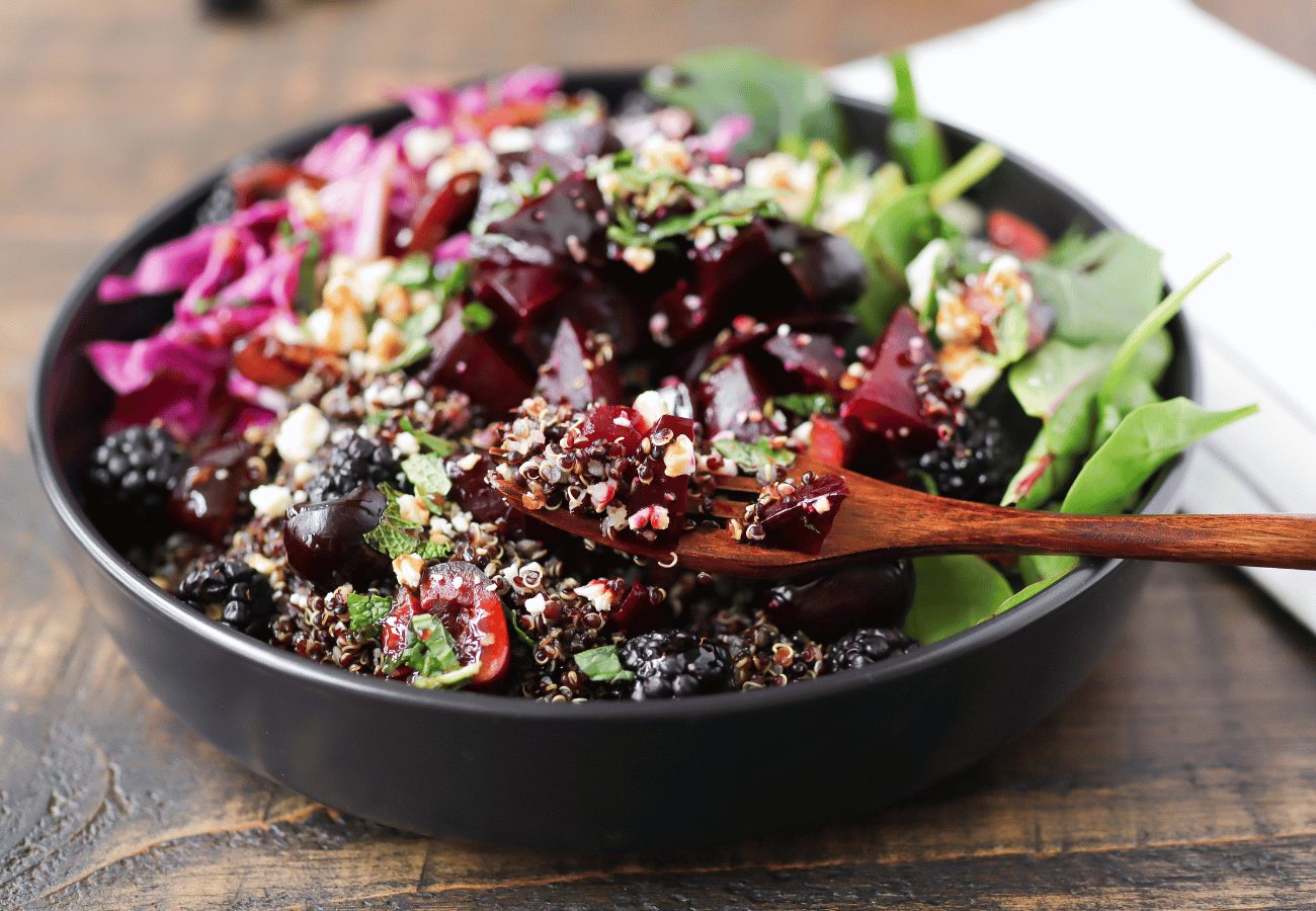 purple vegetables and purple fruits arranged in a black bowl on a wooden table.