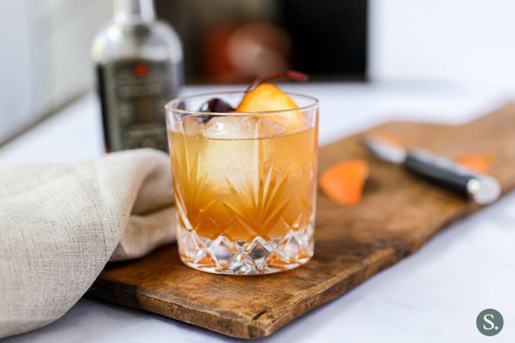 A maple old fashioned mocktail sitting on a cutting board in a low-ball glass