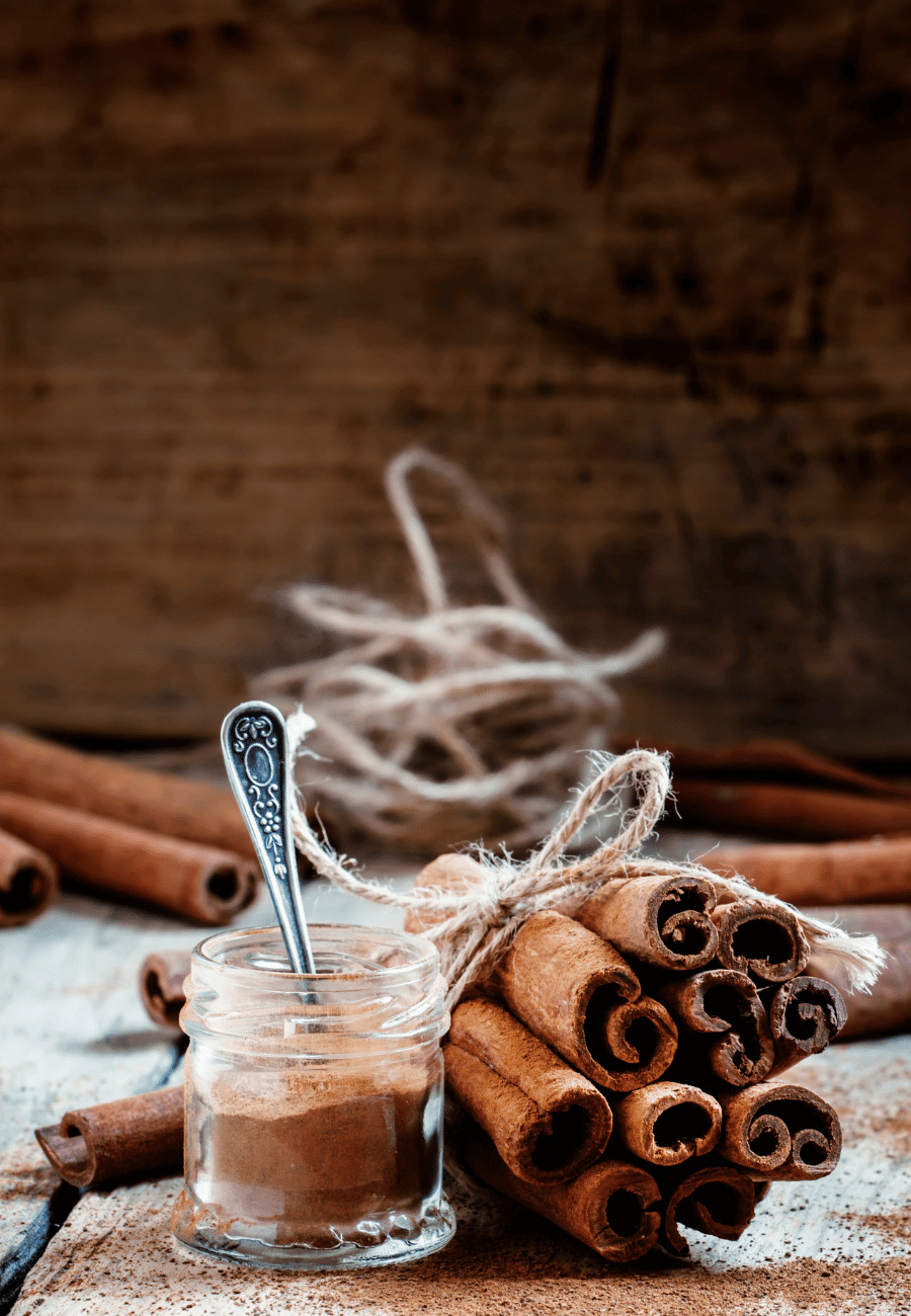 a small jar of cinnamon next to a stack of cinnamon sticks on a dark wood background