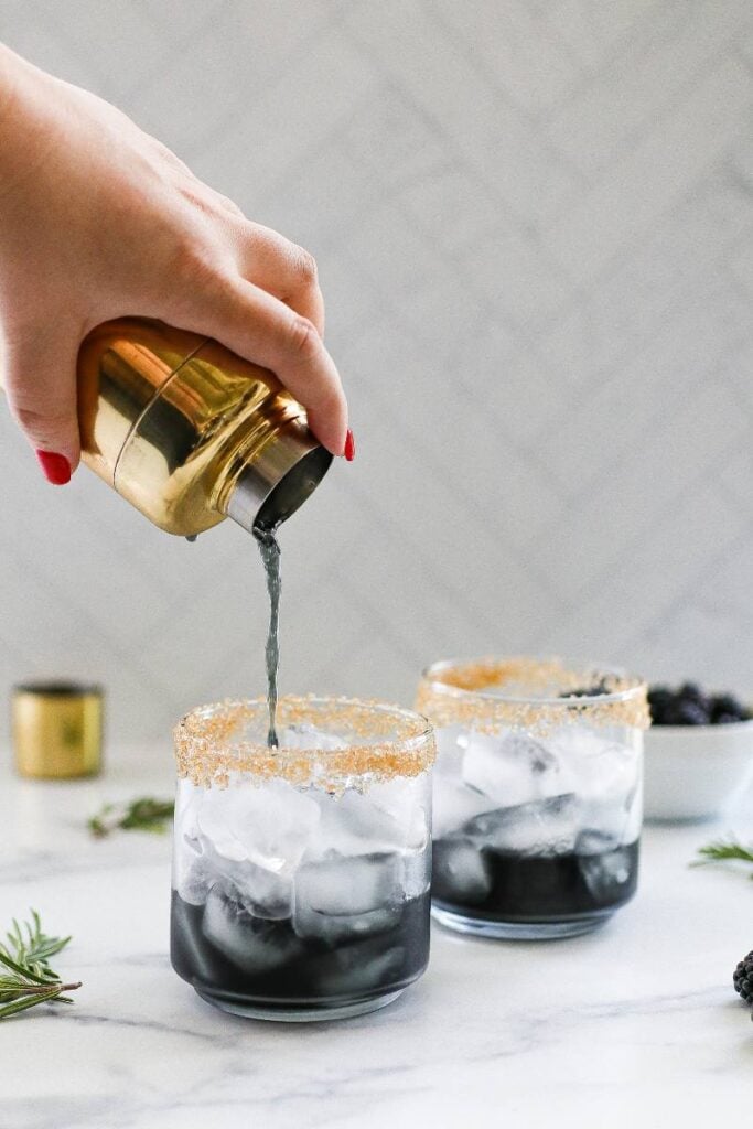 Pouring a purple mocktail mixture from a cocktail shaker into a glass with ice.