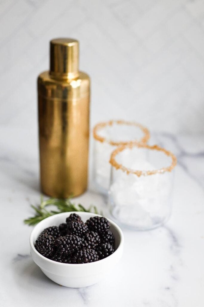 Close up of a turbinado sugar rim on a glass with a fresh blackberry and rosemary garnish.