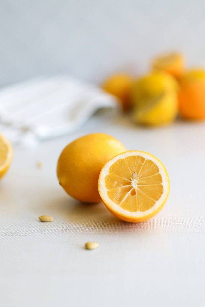 Whole bright yellow Meyer lemons with one cut in half to show the juicy interior and thin white pith.