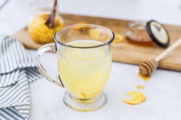 A clear glass mug filled with hot honey citron tea and floating lemon slices, with steam rising.