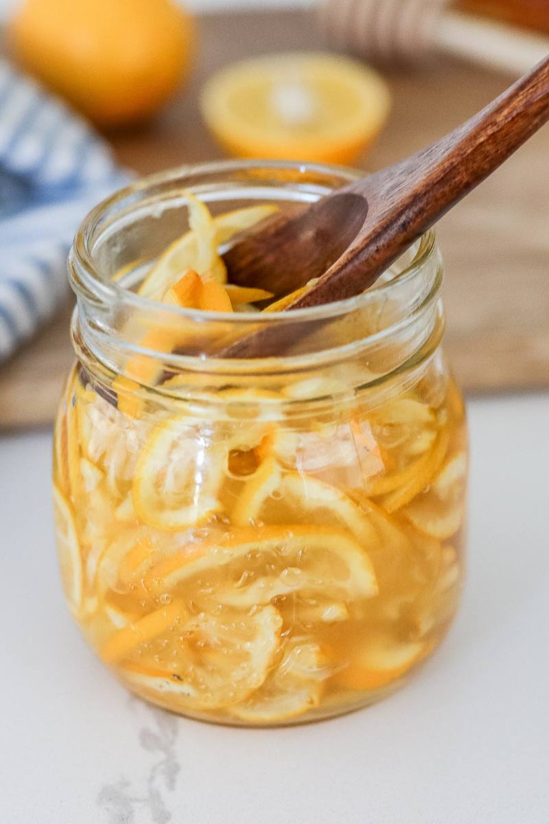 A glass jar filled with homemade honey citron tea marmalade with a spoon lifting out glistening lemon slices.