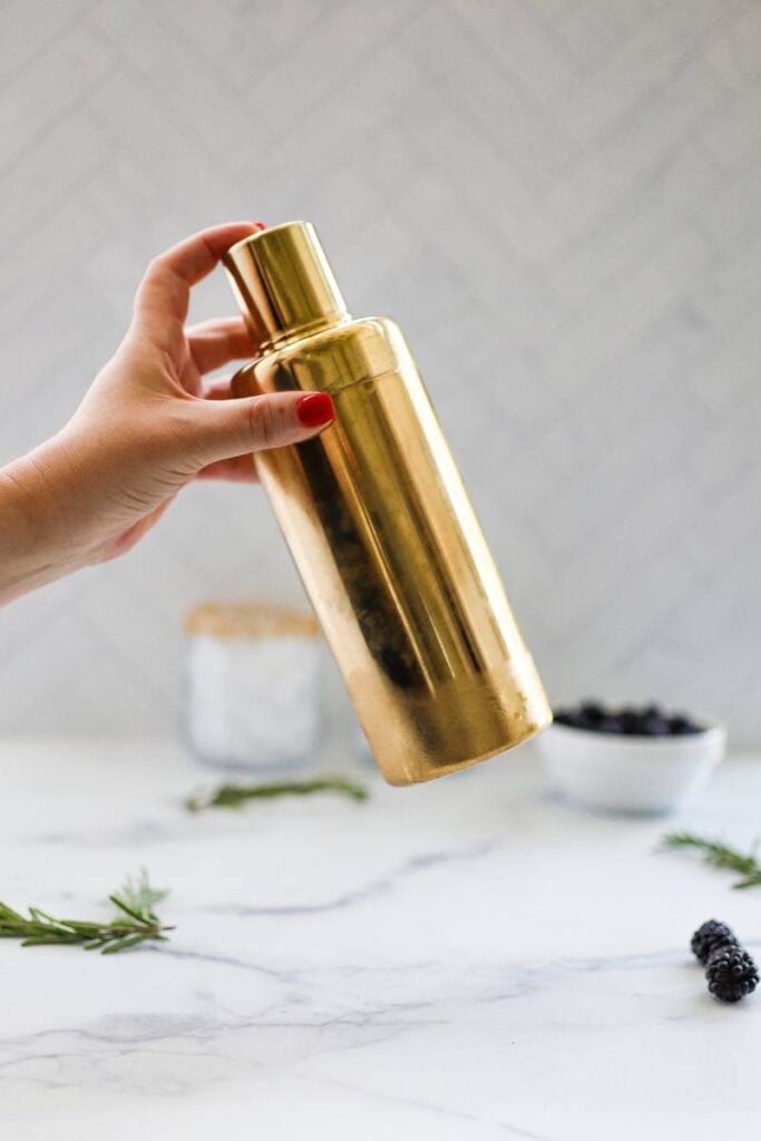 Shaking a purple mocktail mixture with ice before pouring it into sugar-rimmed glasses.
