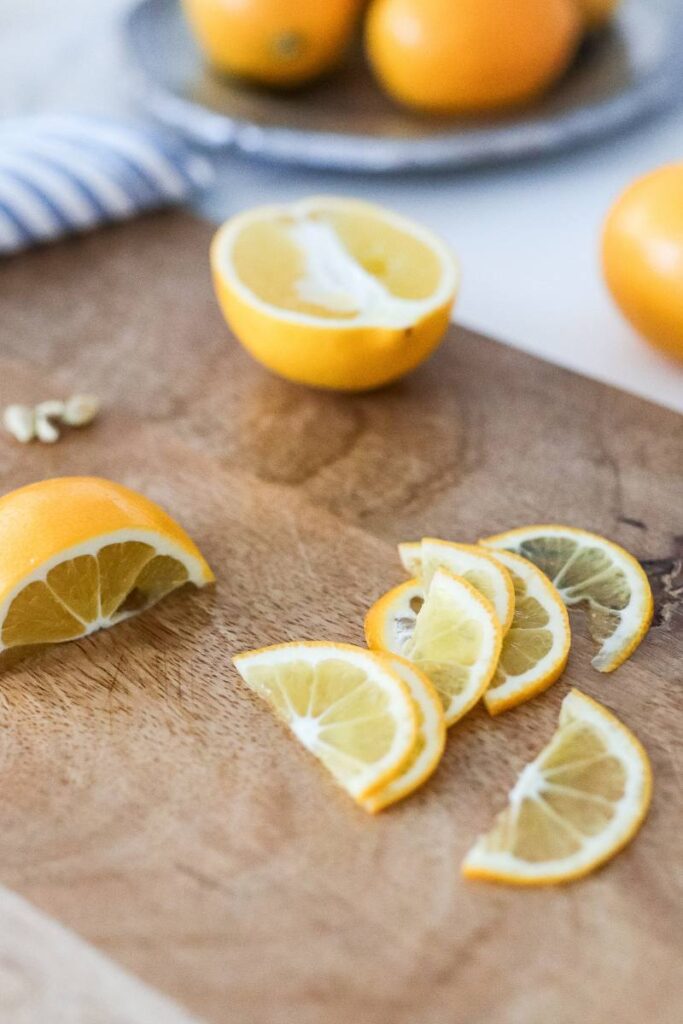 A yellow Meyer lemon sliced into very thin half-moon shapes on a wooden cutting board.
