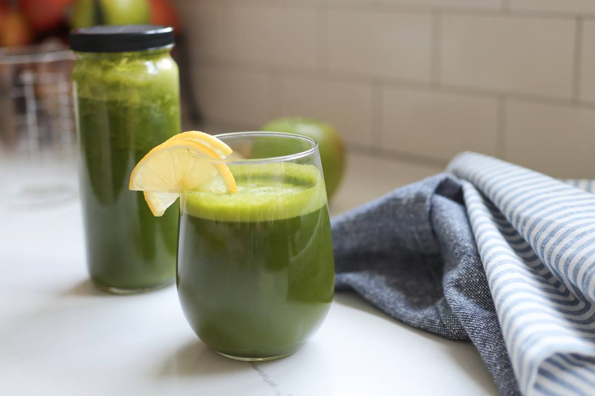 A green smoothie with a yellow slice of lemon sits on a kitchen countertop