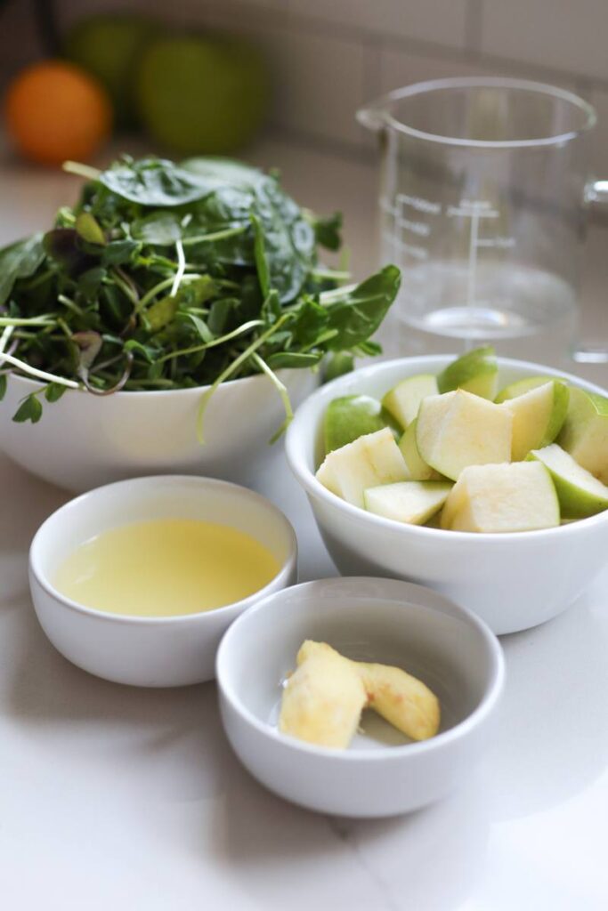 Bowls of spinach, diced green apple, lemon juice and peeled ginger sit on a kitchen countertop.