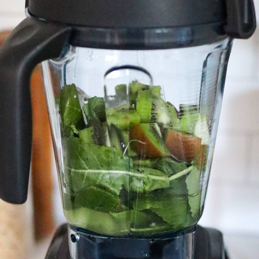 All ingredients layered in a blender: liquids on bottom, fruit and greens on top.